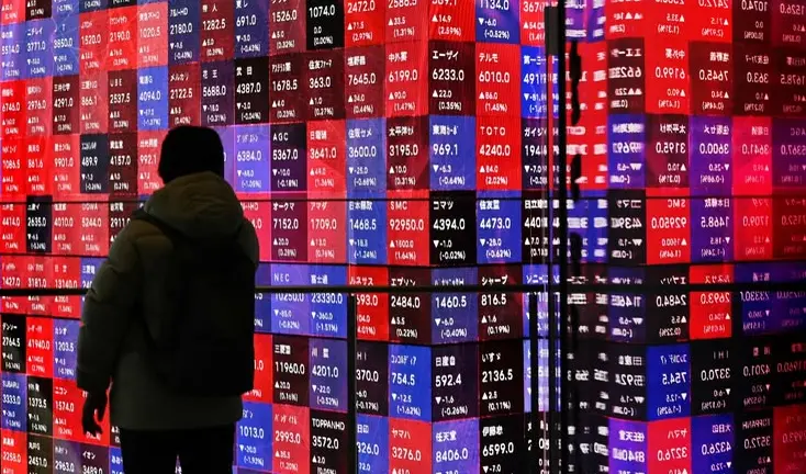 A lone figure silhouetted against a wall-sized stock board of red and blue price tiles.